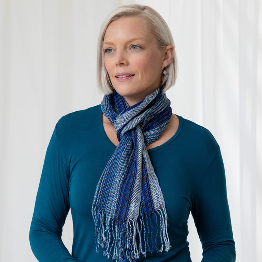A woman wearing a teal shirt and a blue striped alpaca fiber scarf with fringes.