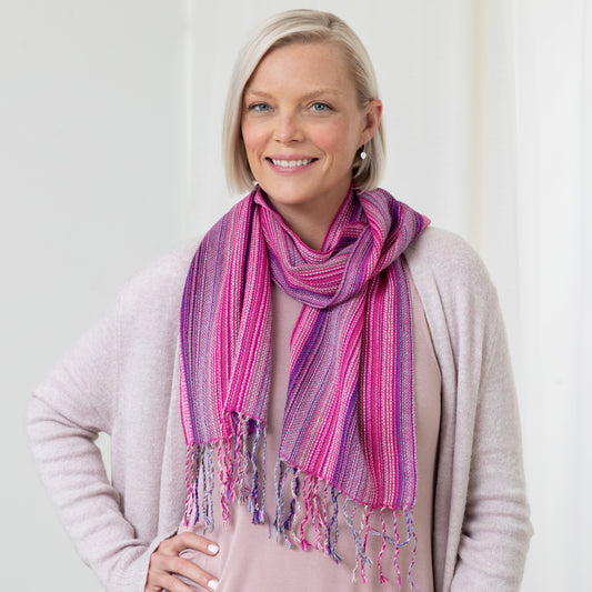 A woman wearing a lavender sweater and a pink and purple, striped alpaca fiber scarf with fringes.