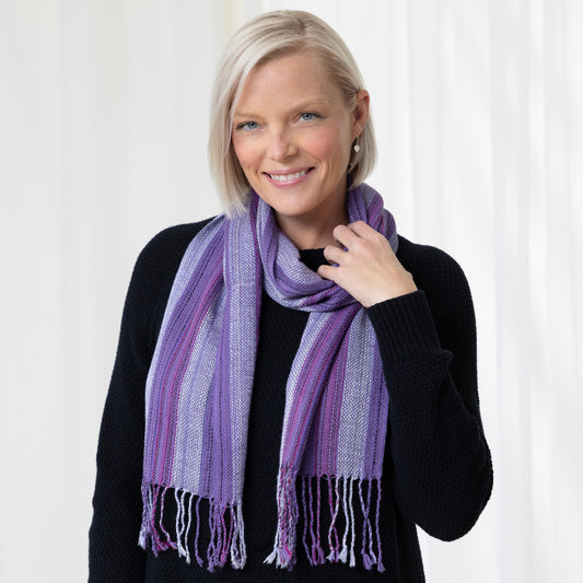 A woman wearing a black shirt and a purple, striped alpaca fiber scarf with fringes.