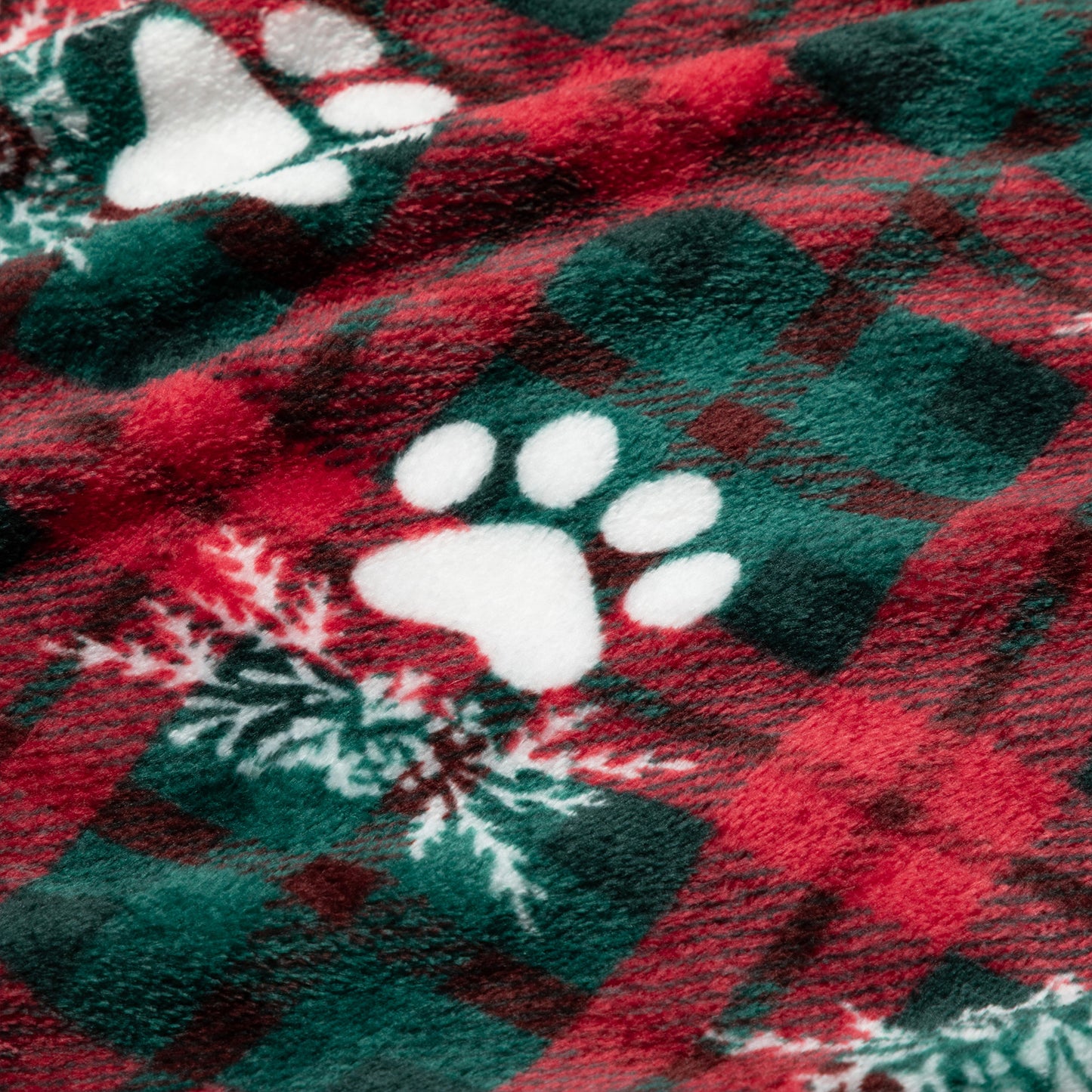 Close-up of a red and green plaid fabric with white paw prints and snowflakes.