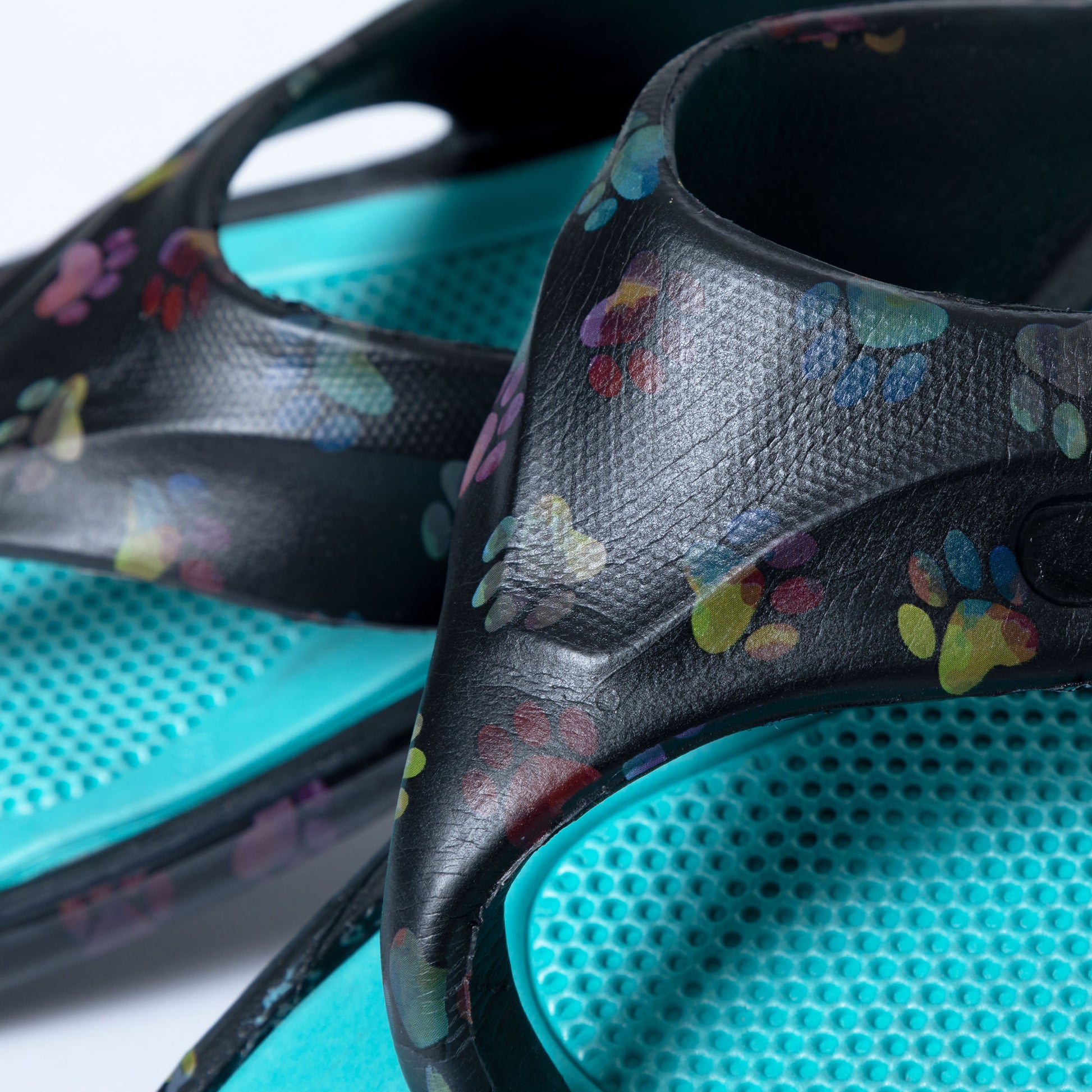 A detail image of pair of rainbow ombre paw EVA flip flops on white background The Rainbow Ombre Paw print is on a black background with a teal bright blue textured foot bed