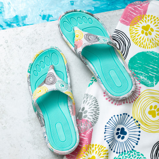 Colorful flip-flops placed beside a patterned beach towel near a pool.