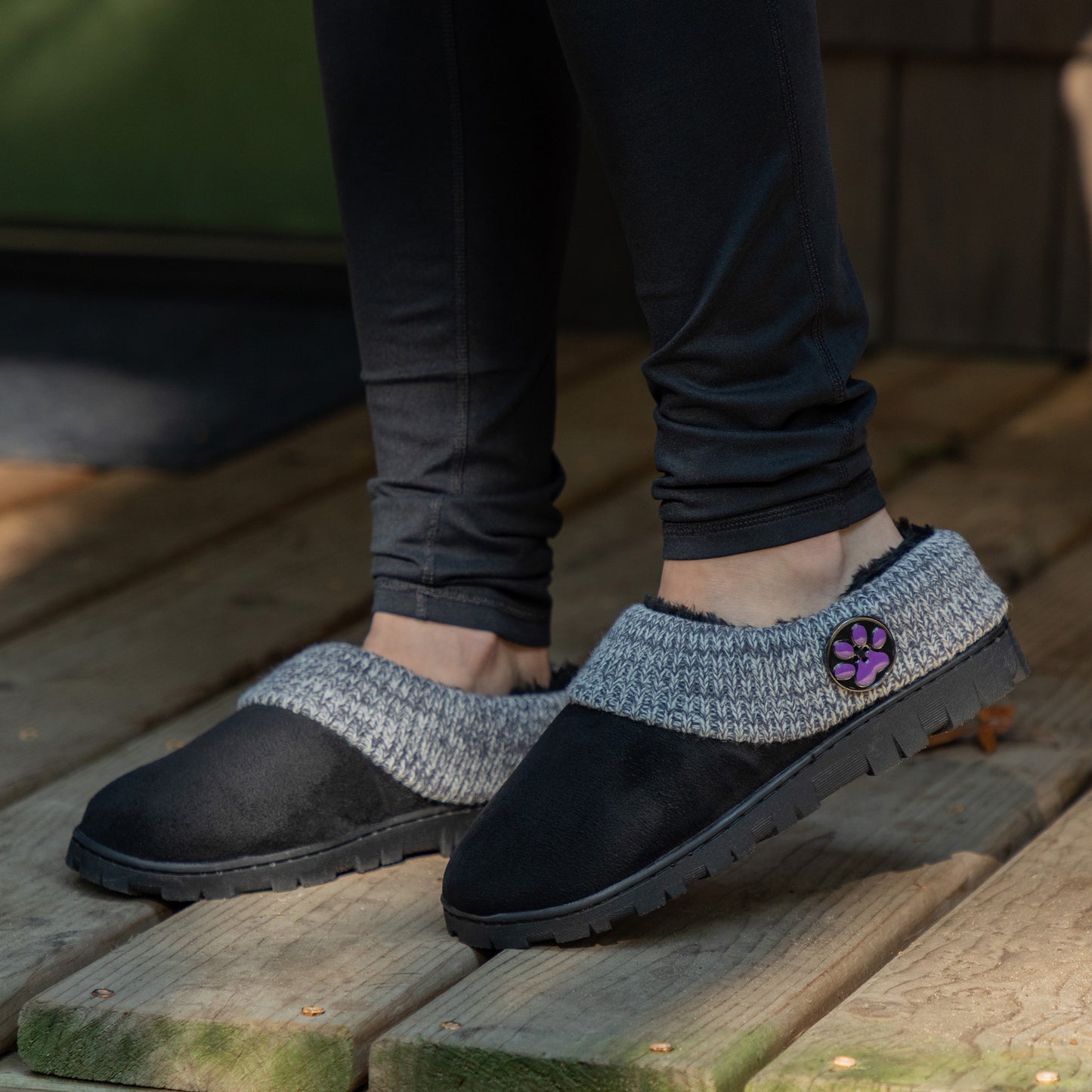 Person wearing black and gray slippers with a paw print on a wooden floor