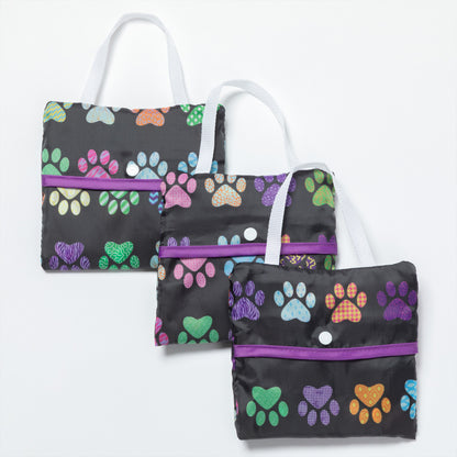 Three folded compact reusable bags with colorful paw prints all over, against a white background.