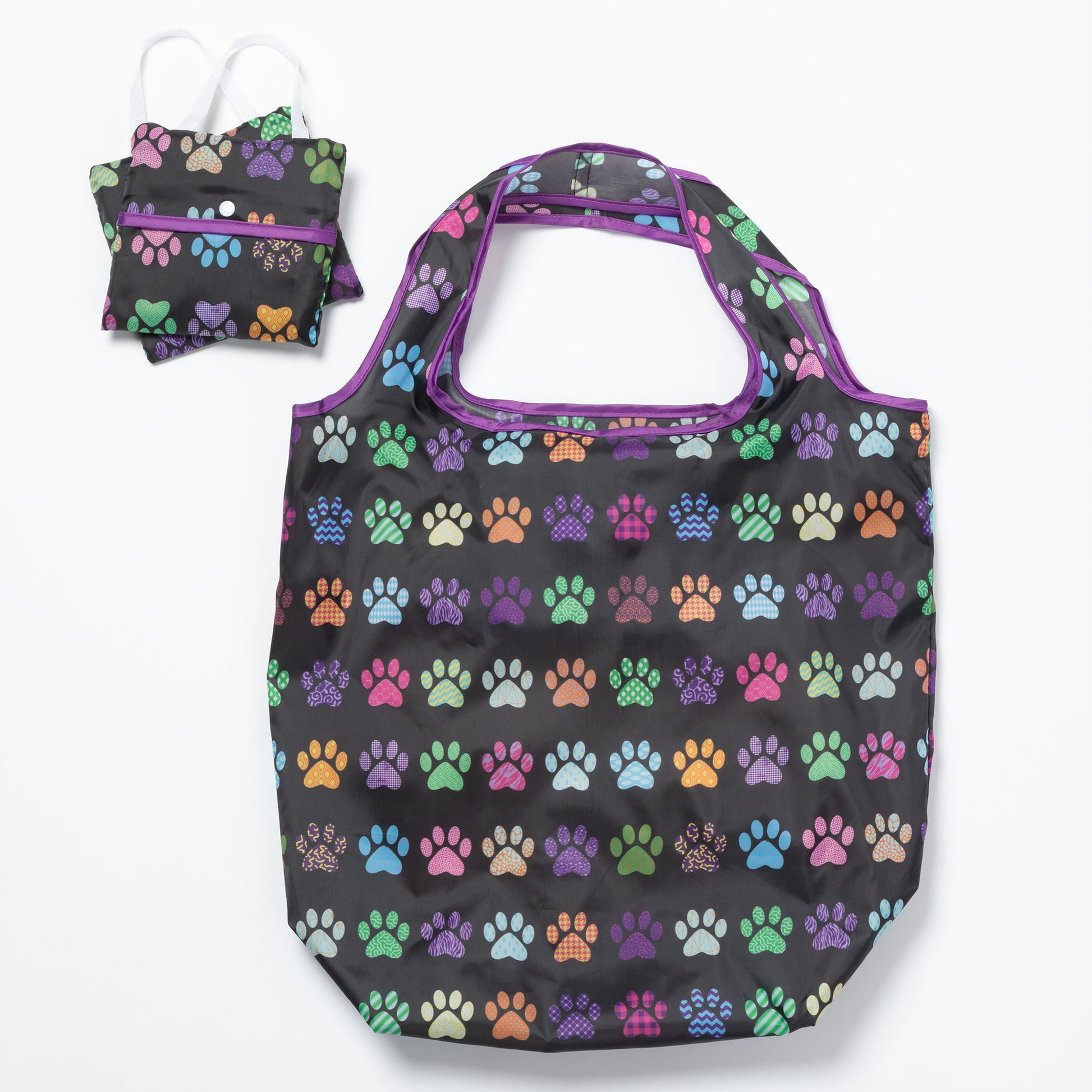 A black reusable bag with colorful paw prints all over, and two folded bags compact next to it, on a white background.