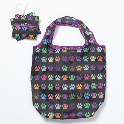 A black reusable bag with colorful paw prints all over, and two folded bags compact next to it, on a white background.
