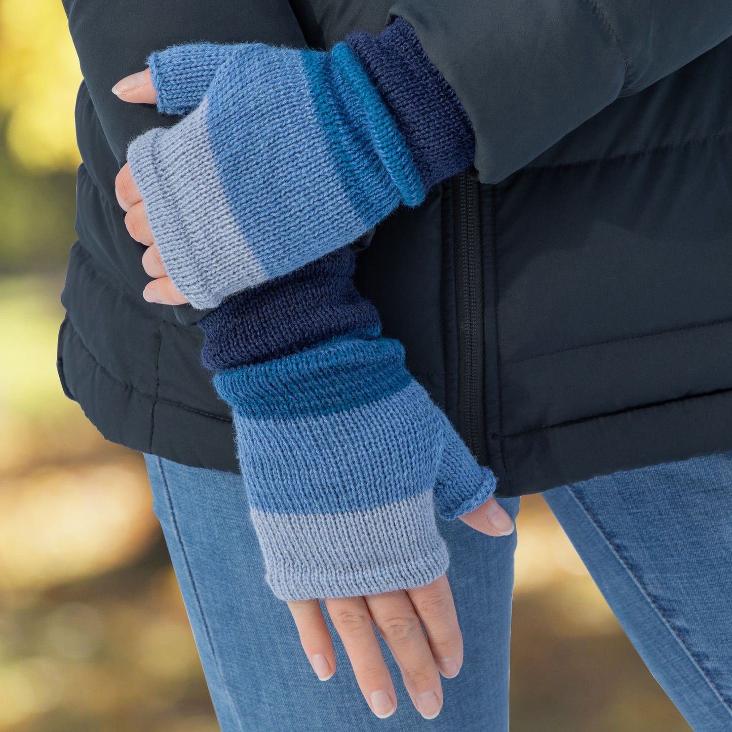 Person wearing blue striped fingerless gloves with a blurred outdoor background