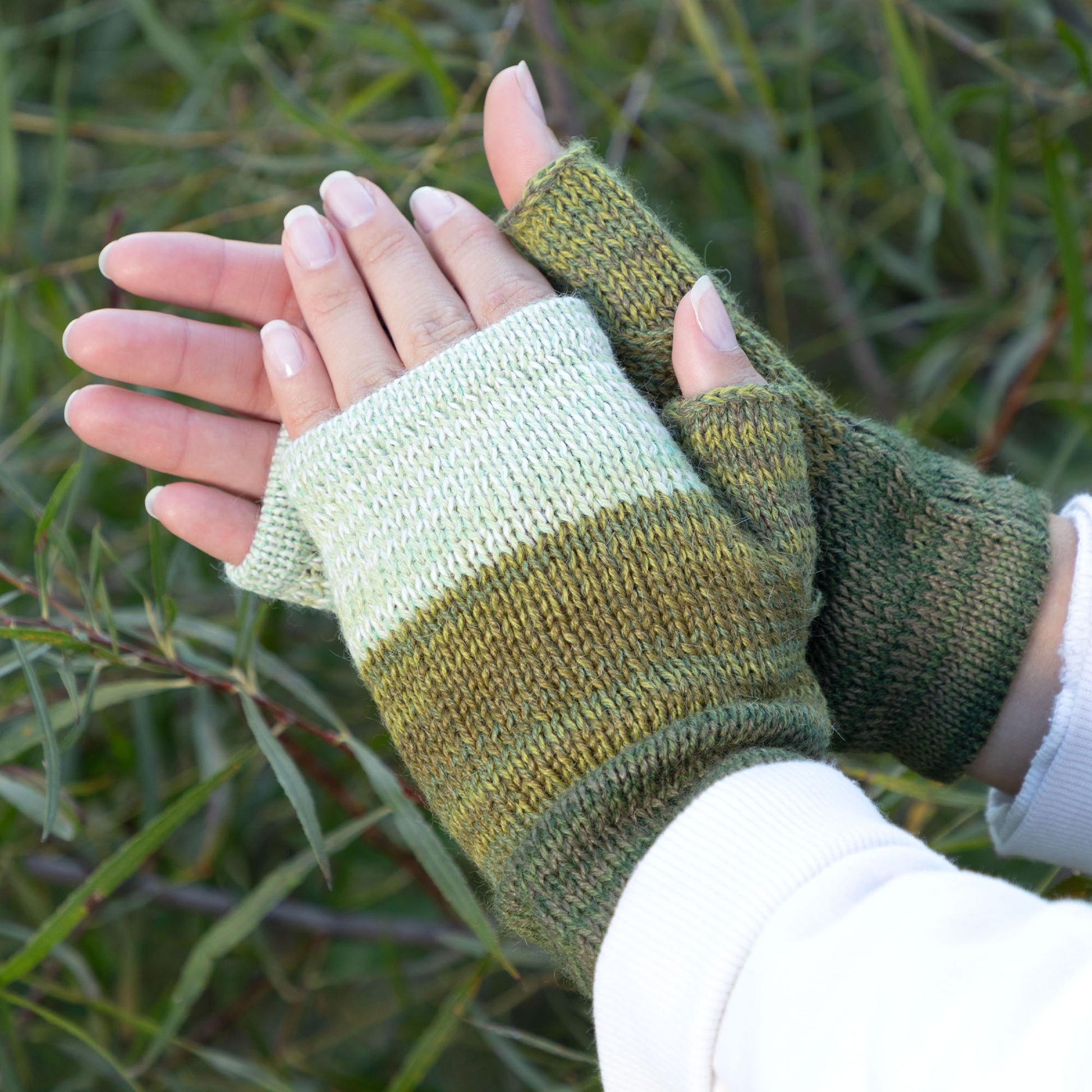 Green and beige striped fingerless gloves worn outdoors with greenery in the background