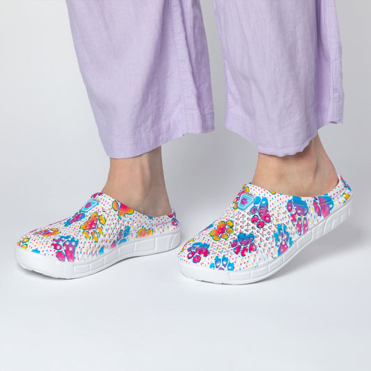 Colorful, patterned clogs worn with light purple pants in a simple setting.