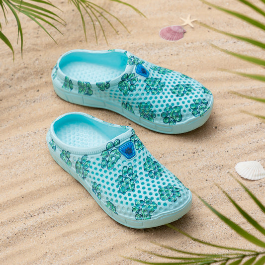 Turquoise slip-on clogs with green floral patterns on sandy beach backdrop.