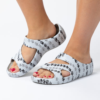 White sandals with black paw prints worn by a person on a white background