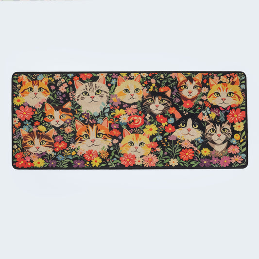 A rectangular mat featuring a dense, colorful illustration of various cat faces surrounded by flowers on a dark background, shown against a plain light gray studio backdrop.