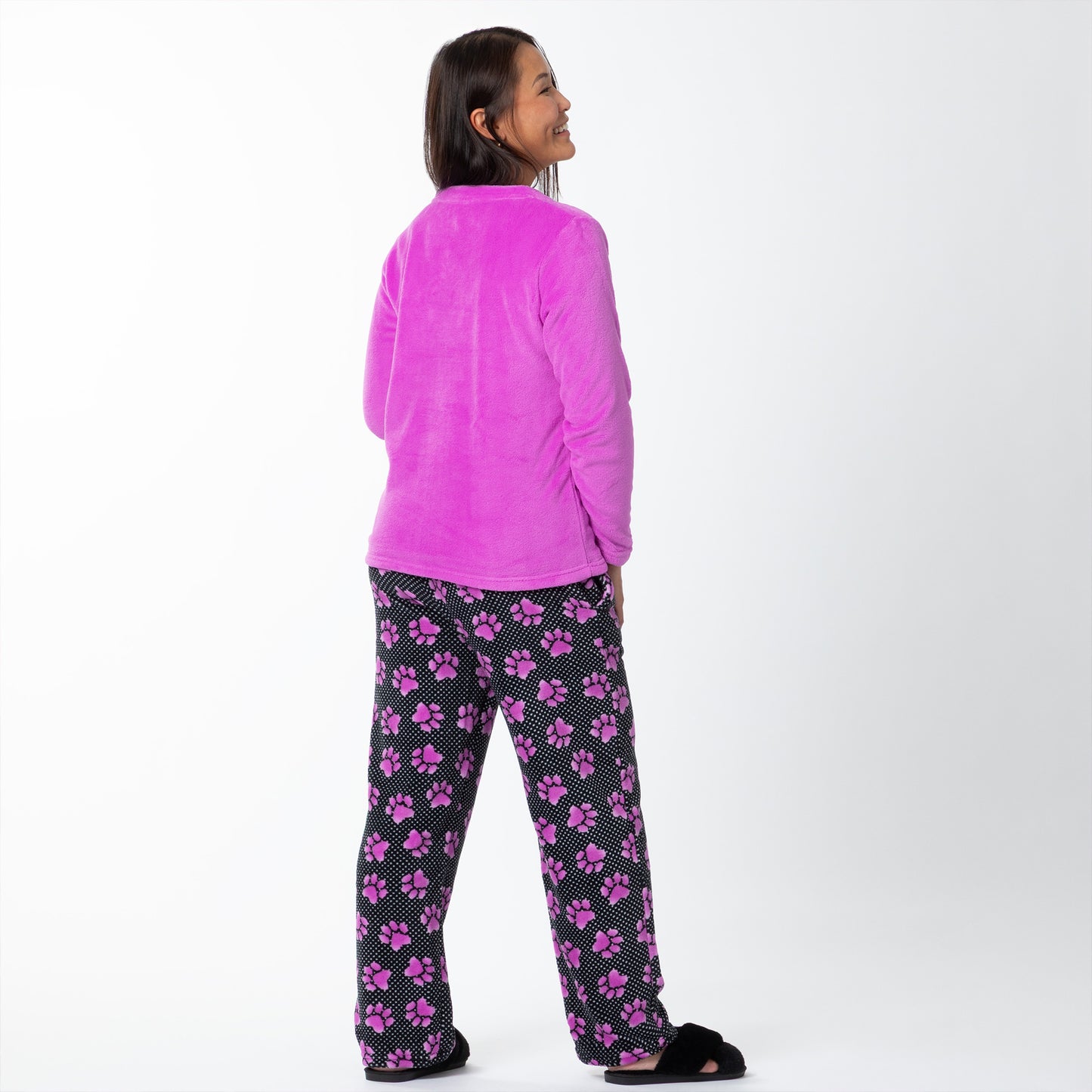 A woman wearing a soft magenta long-sleeve shirt and a pair of soft black pants patterned with white polka dots and magenta paw prints, showing the back of the top and bottoms. 