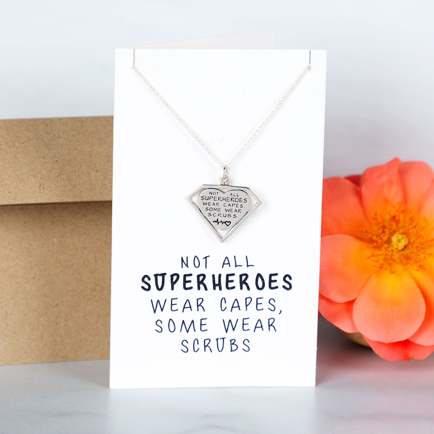 Necklace with pendant on a card with text, next to a flower and envelope