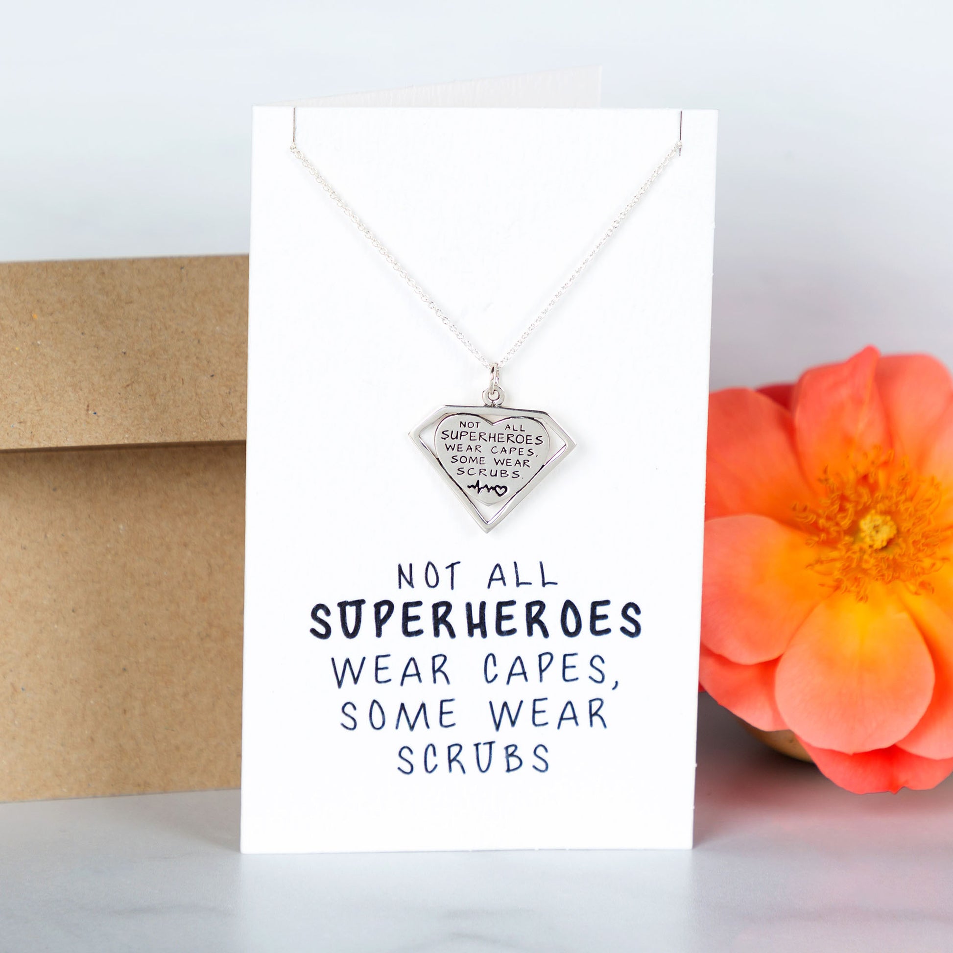 Necklace with pendant on a card with text, next to a flower and envelope