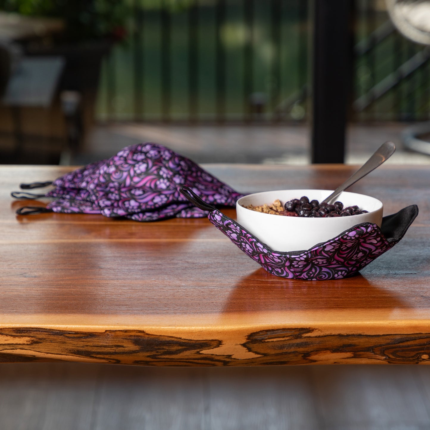 Purple paw symphony bowl cozy on a wooden table with a bowl of food and spoon