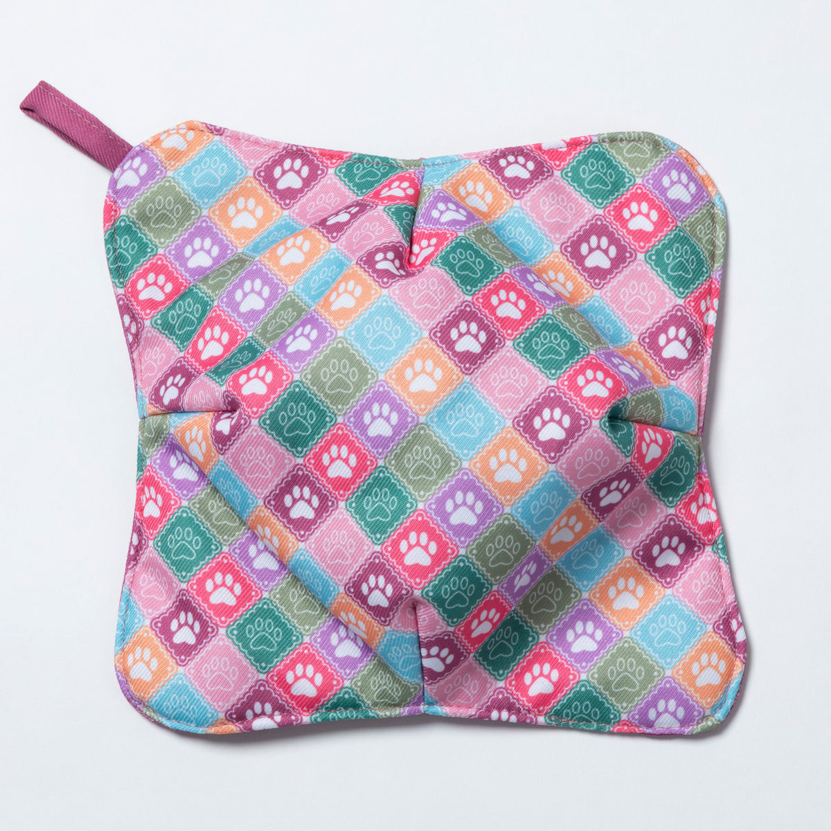 A square quilted fabric potholder with a colorful diamond pattern featuring paw prints in pink, purple, orange, green, and blue on a light pink background, with a matching fabric handle.