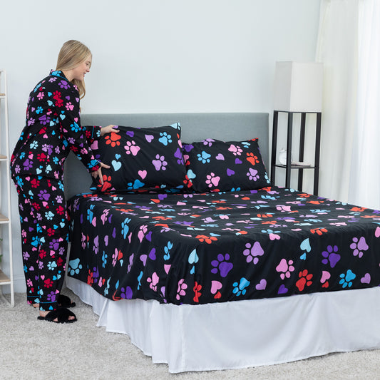 Hearts and Paws black microfiber sheet set fitted to queen size bed in bedroom setting. Model is dressed in matching set and fluffing pillows