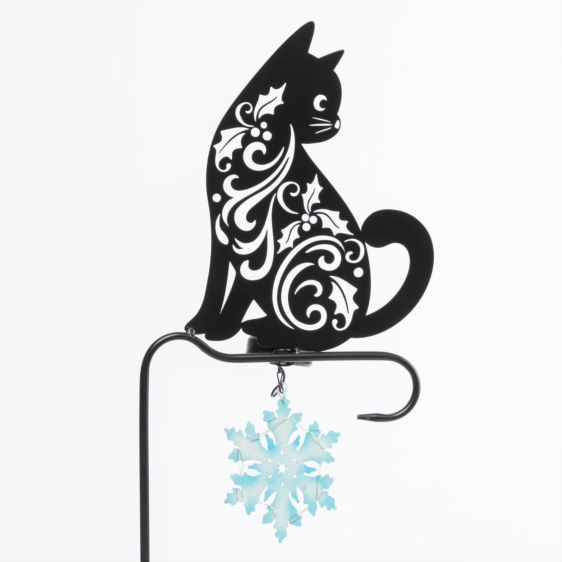 Decorative black cat with white patterns on a stand with a blue snowflake ornament against a white background