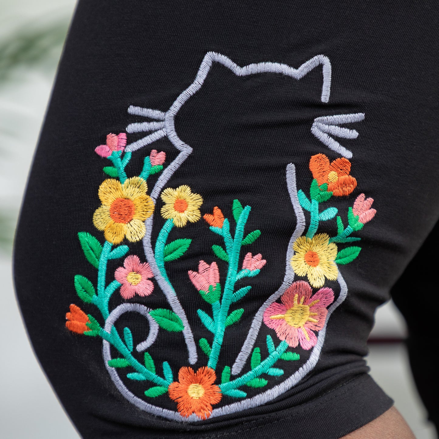 Embroidered design of a cat with flowers on a black pair of stretch capris.