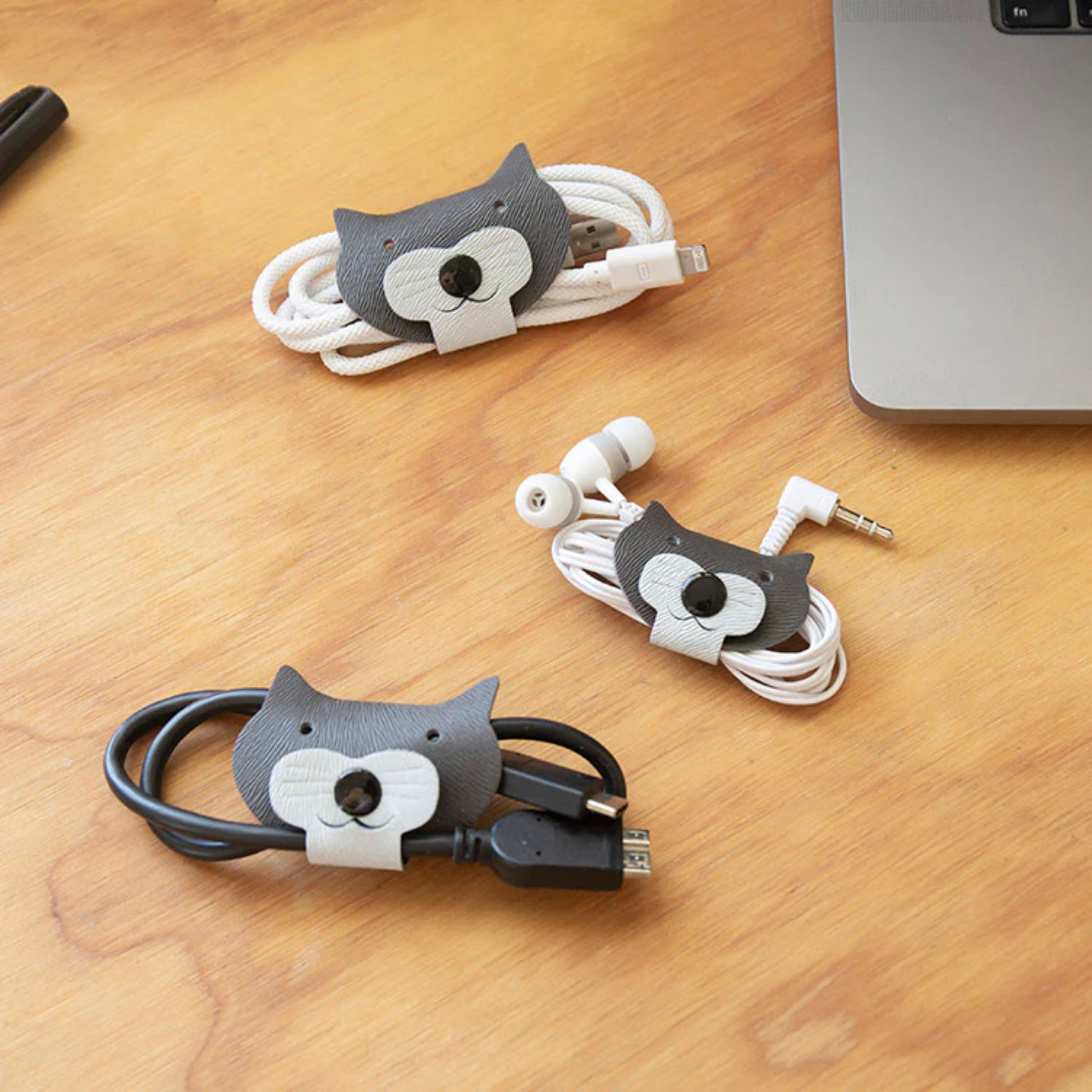 Cable organizers shaped like cats on a wooden surface with electronic devices.