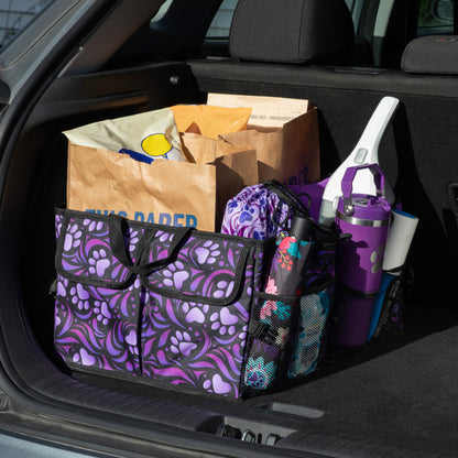 A purple paw printed car trunk organizer, in a car trunk, filled with grocery bags, water bottle, umbrella, and other items.