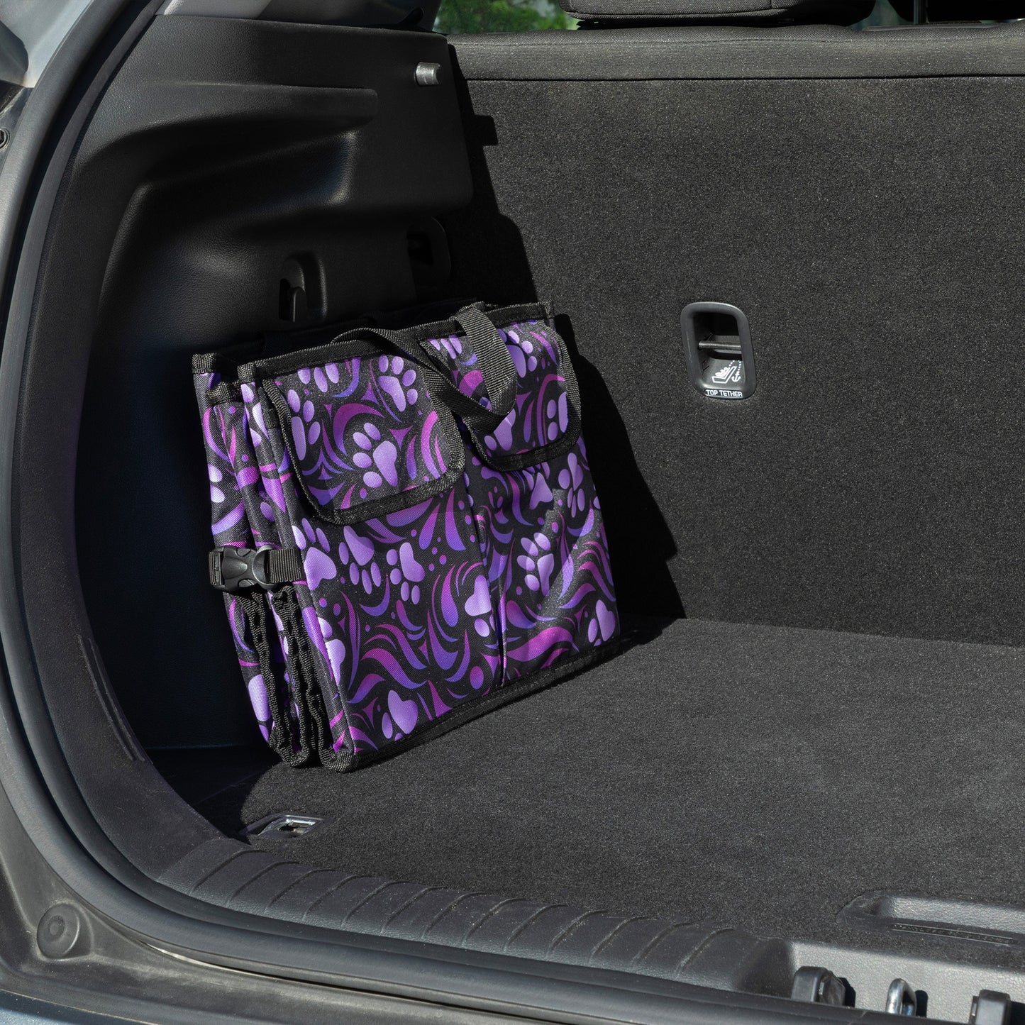 A purple paw print patterned car trunk organizer folded flat, in a car trunk.