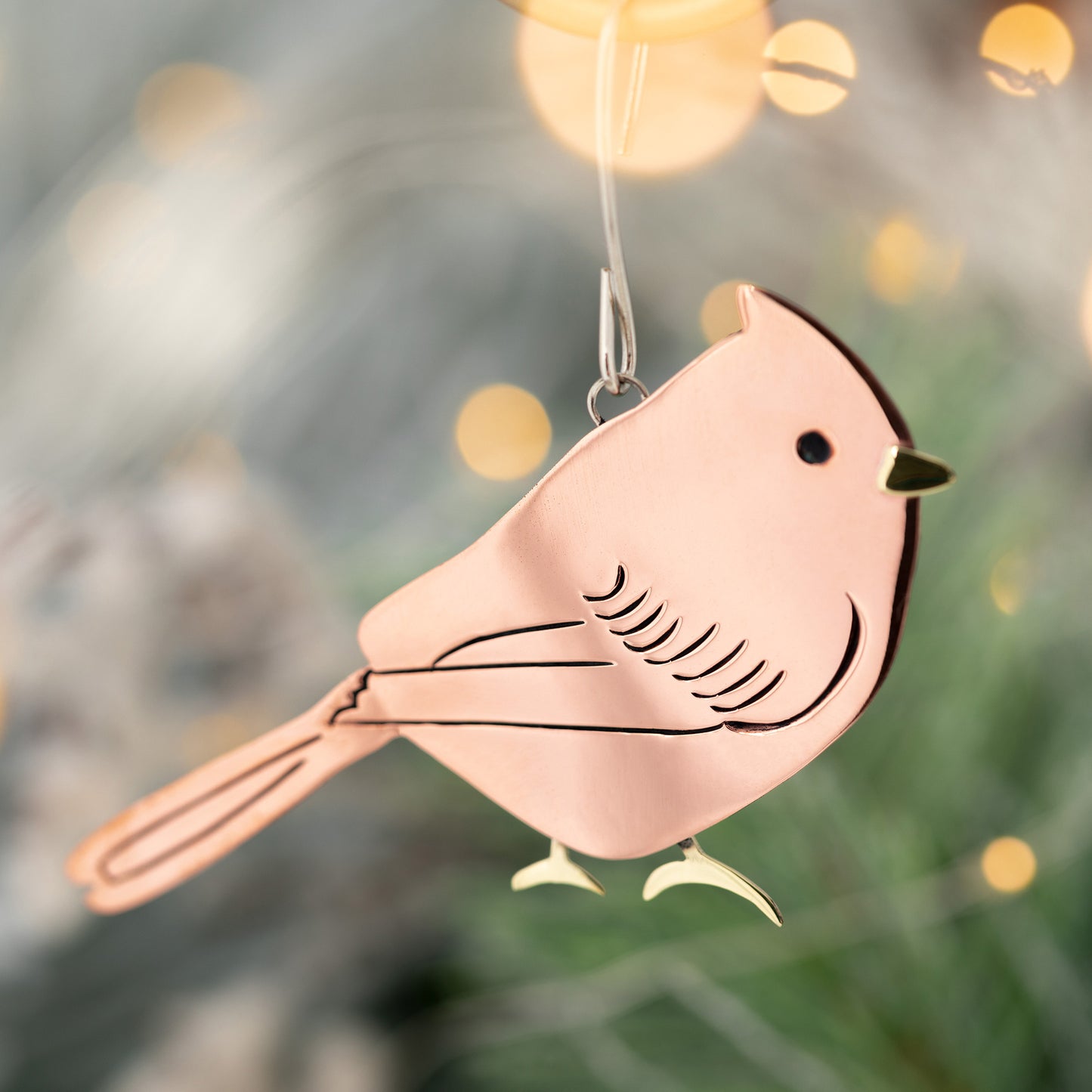 Decorative bird ornament hanging against a blurred Christmas tree background.