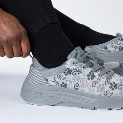 Person putting on a gray paw print patterned running shoe with black socks.