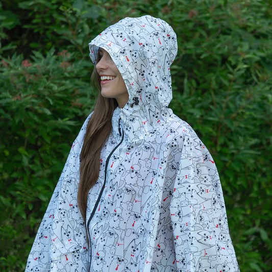 Person wearing a white hooded poncho with dogs all over, with a leafy green background.