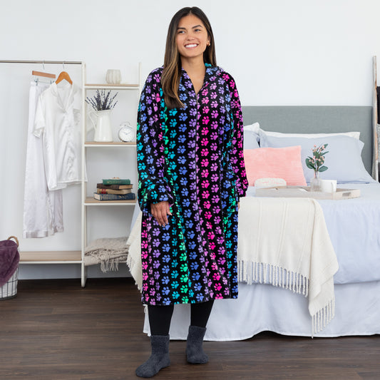 Woman in a rainbow paw print patterned blanket hoodie in a bedroom setting.
