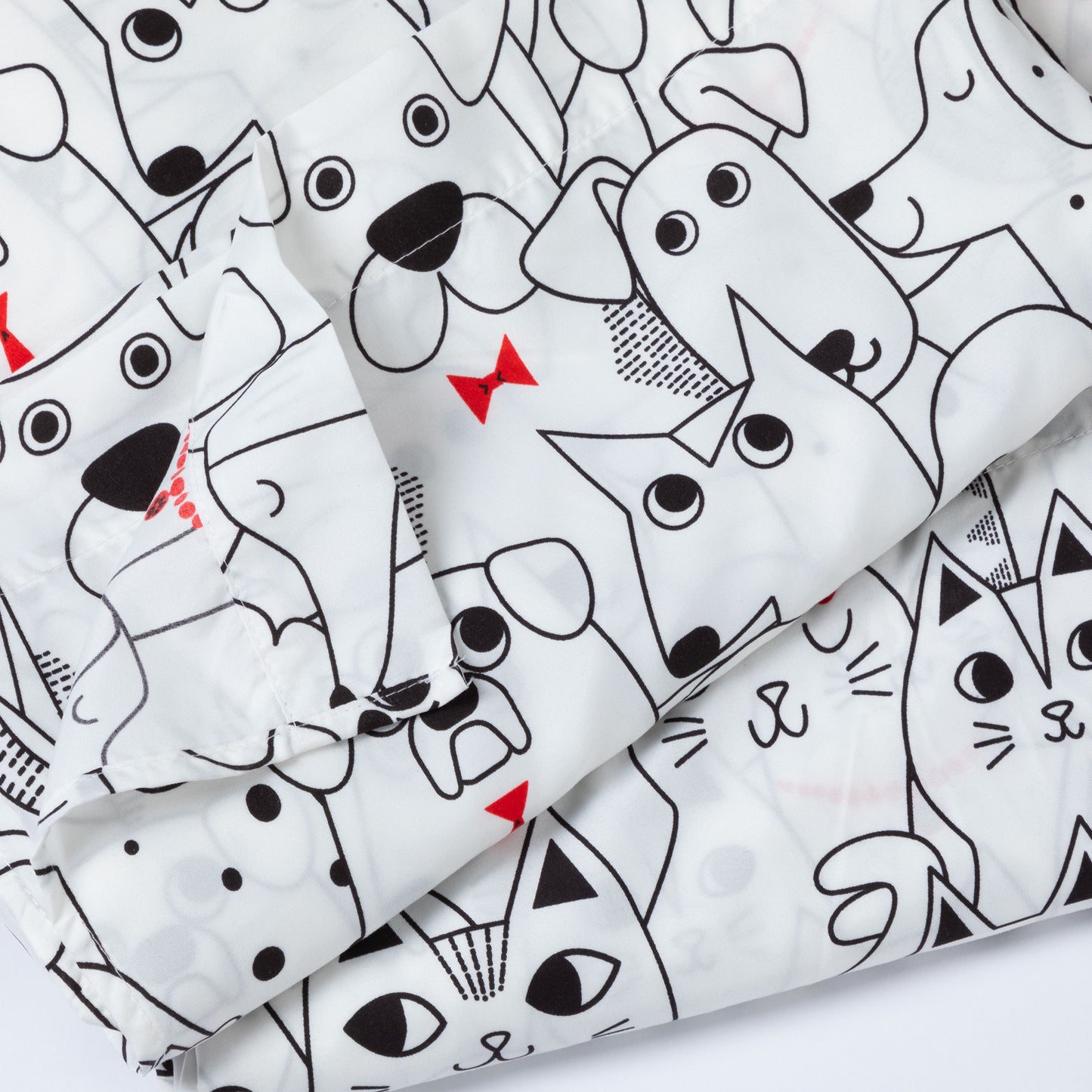 A close-up of a white fabric item, likely a blanket or quilt, featuring a playful cartoon print of various dog and cat faces in black line art with small red accent details.