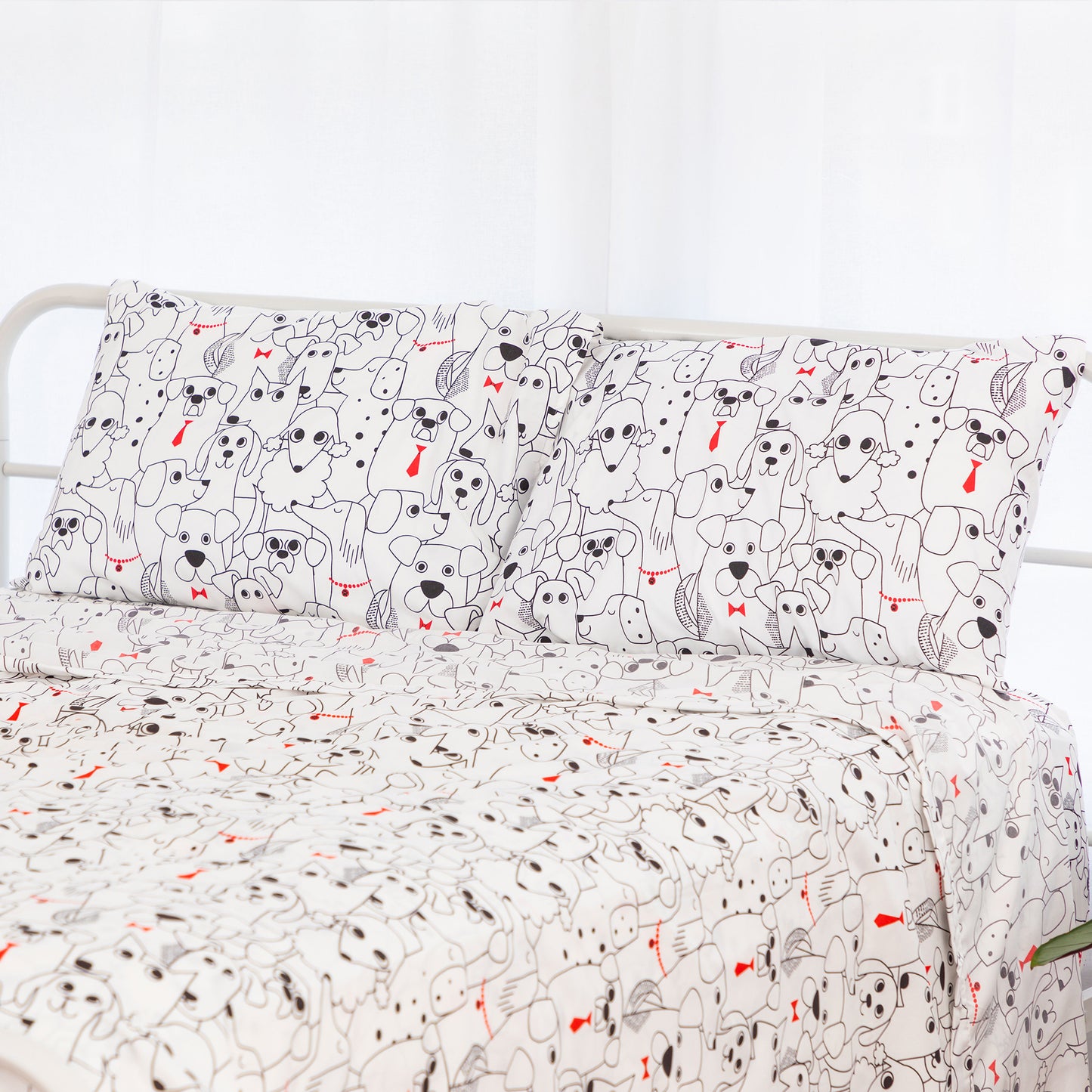 A bed dressed in a white bedding set with a repeating cartoon dog print in black and small red accents, shown against a bright white background.