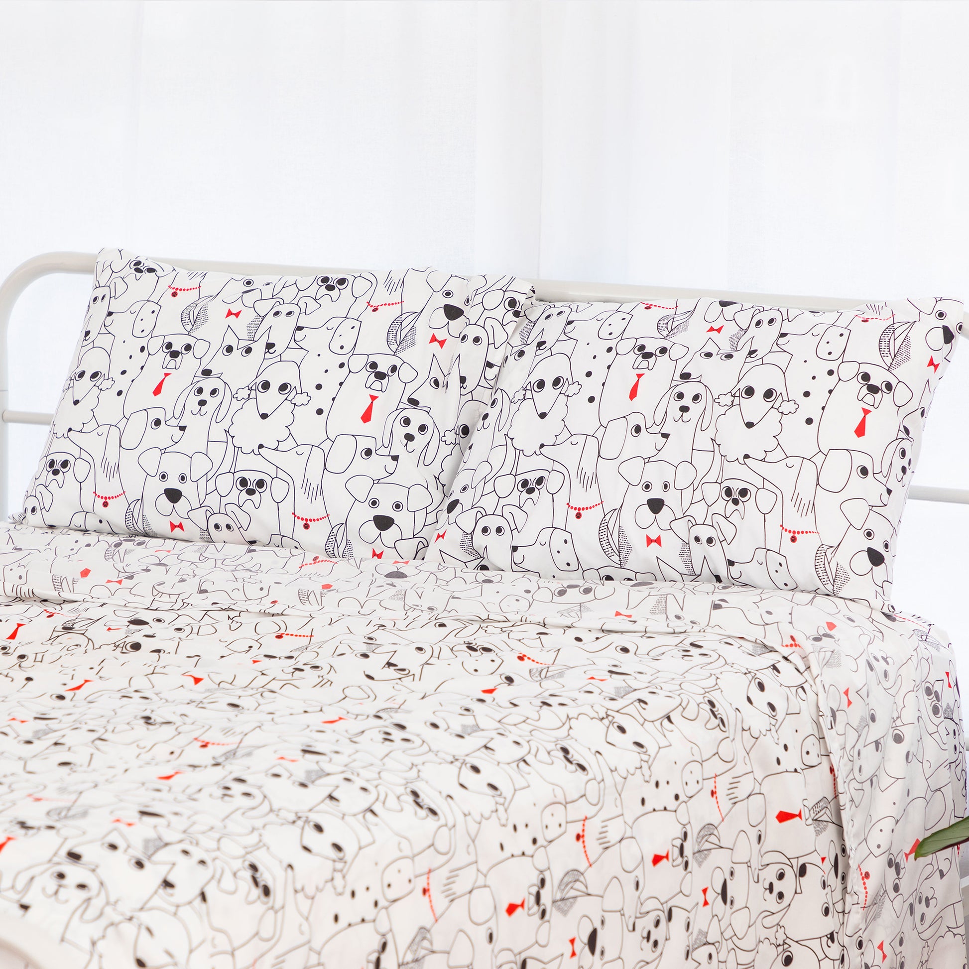 A bed dressed in a white bedding set with a repeating cartoon dog print in black and small red accents, shown against a bright white background.
