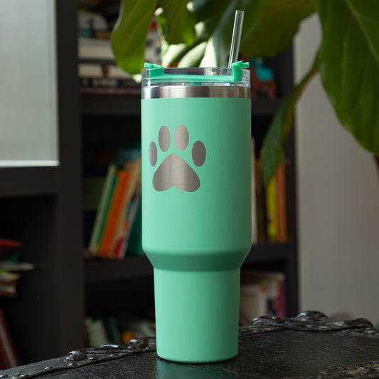 Turquoise 40 oz tumbler with paw print design on a surface with a blurred background.