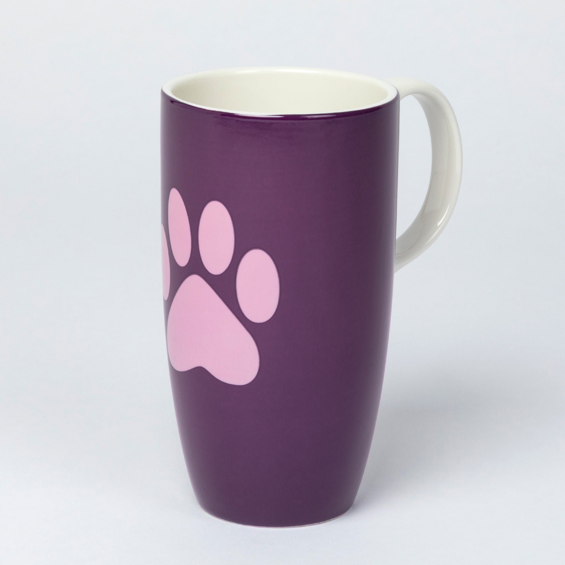 A tall ceramic mug with a purple exterior, a pink paw print graphic, and a white handle and interior, shown on a light gray background.