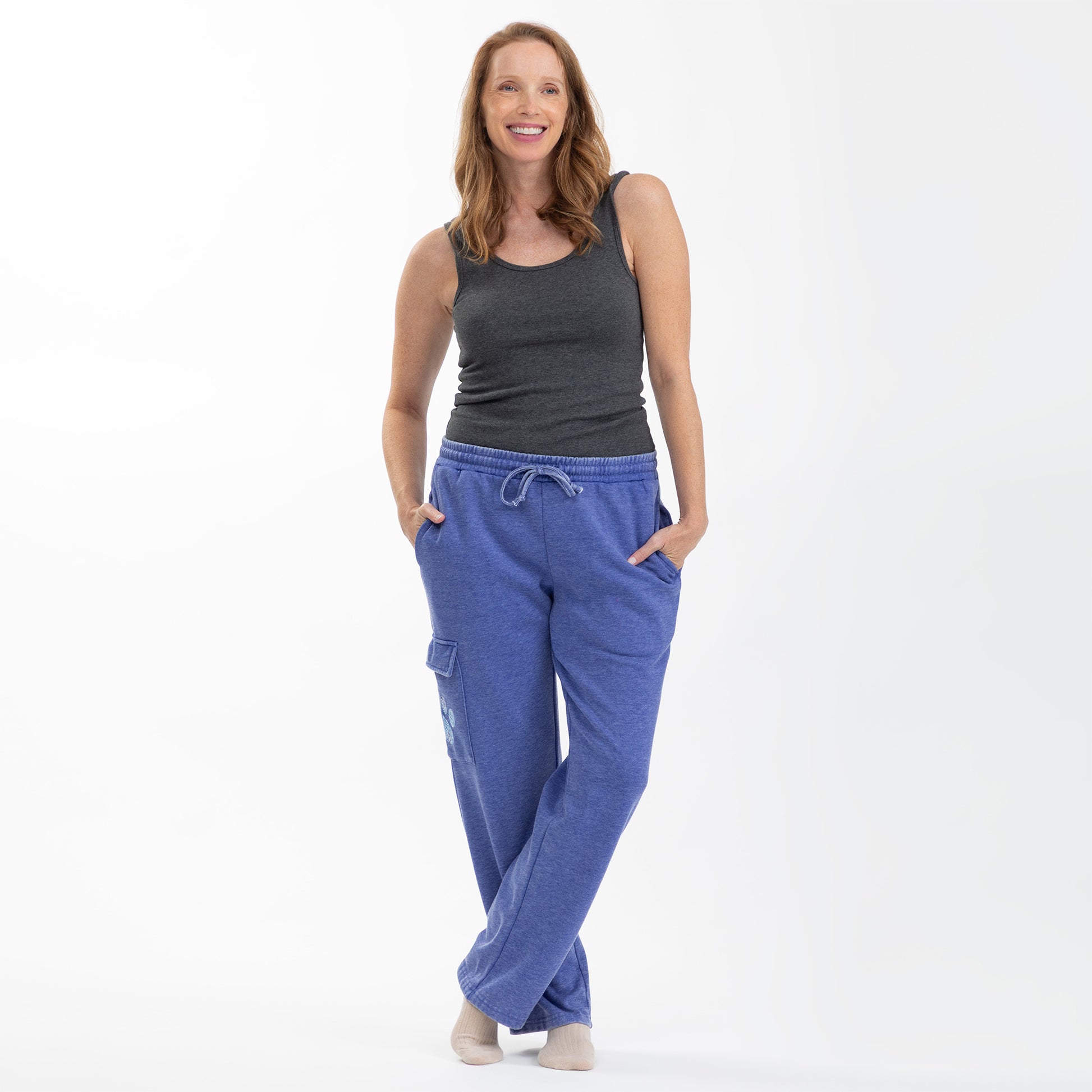 A woman modeling a gray tank top and blue cargo-style pants, standing against a white background.