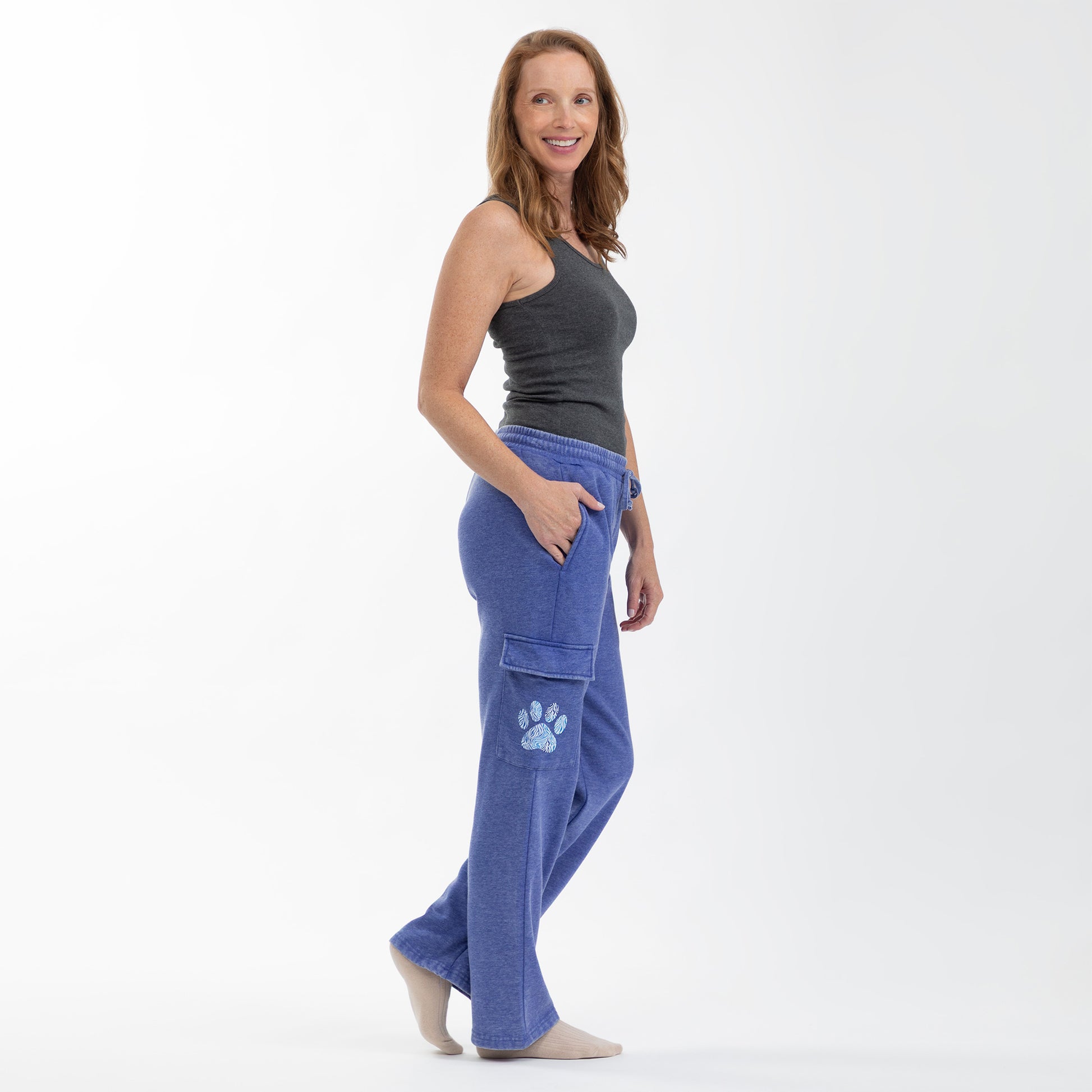 A woman modeling a gray tank top and blue cargo-style pants, standing against a white background.