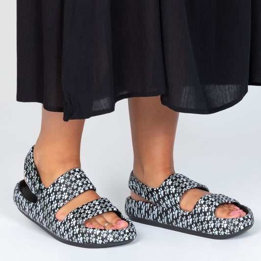 Close-up of feet in stylish black and white paw patterned sandals, wearing a black dress.