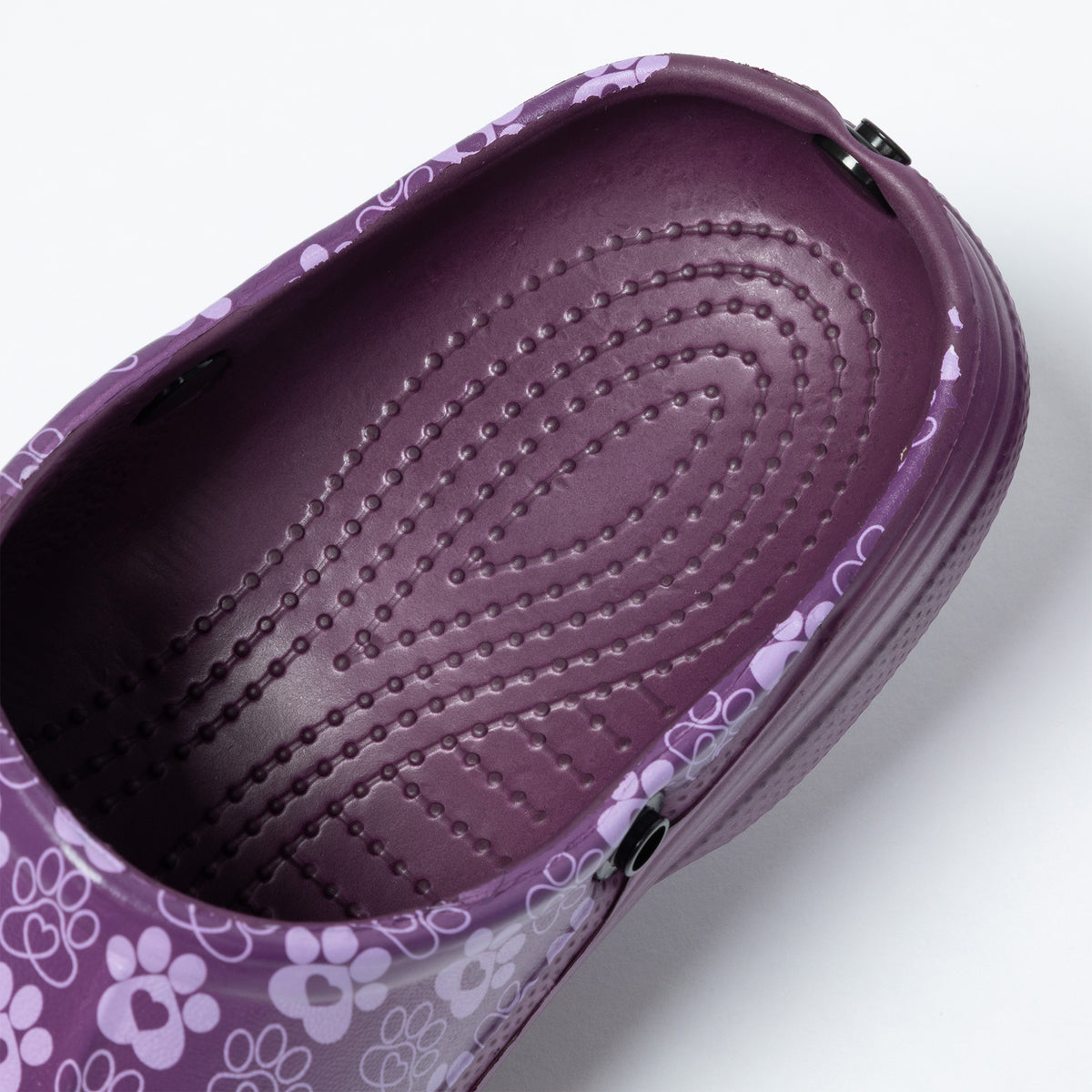 A close-up of a purple clog shoe with a floral and paw-print pattern on the side and a textured, raised-dot footbed.