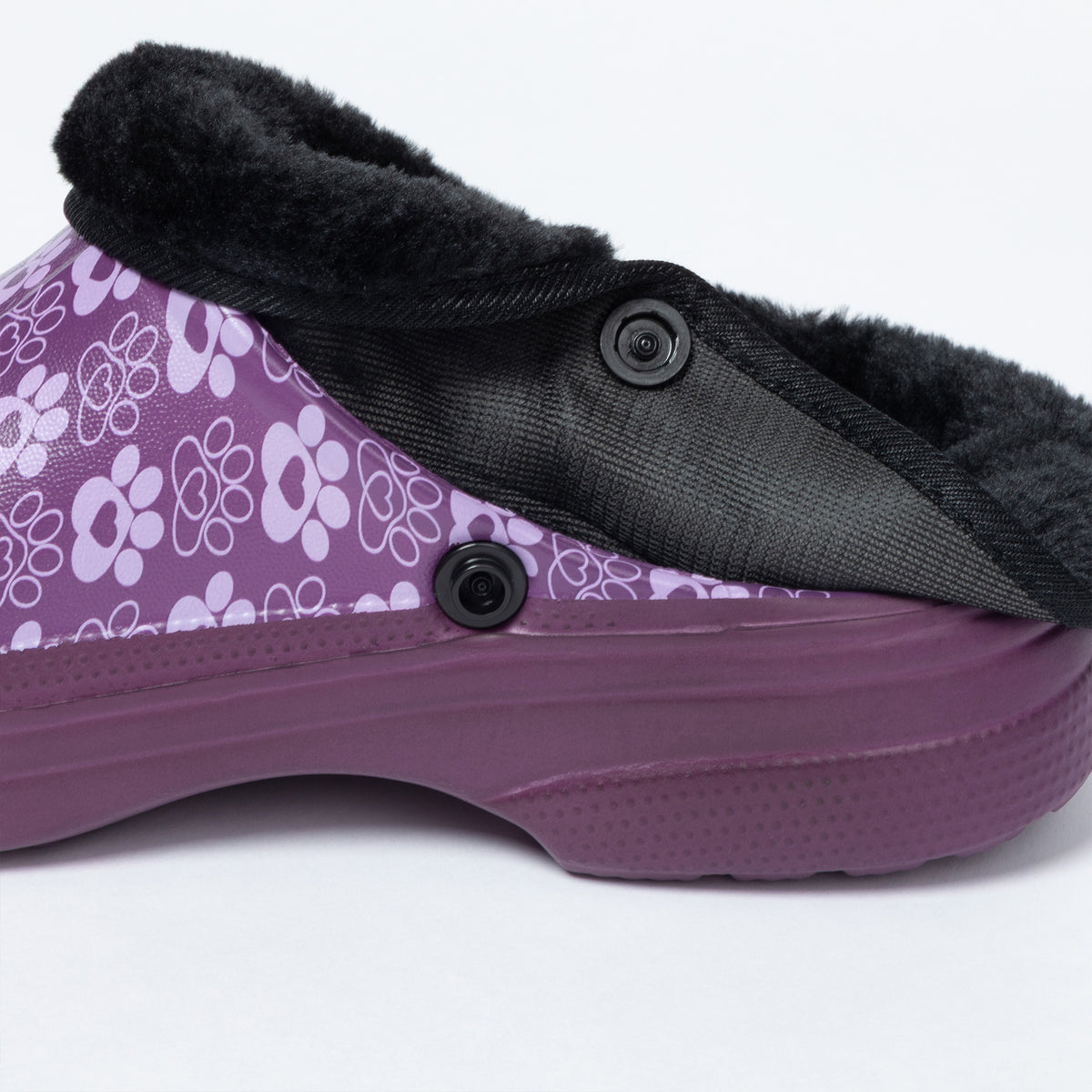 A close-up side view of a purple slip-on clog shoe with a black faux-fur collar, black buttons, and a purple sole on a white background.