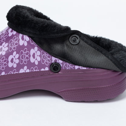 A close-up side view of a purple slip-on clog shoe with a black faux-fur collar, black buttons, and a purple sole on a white background.