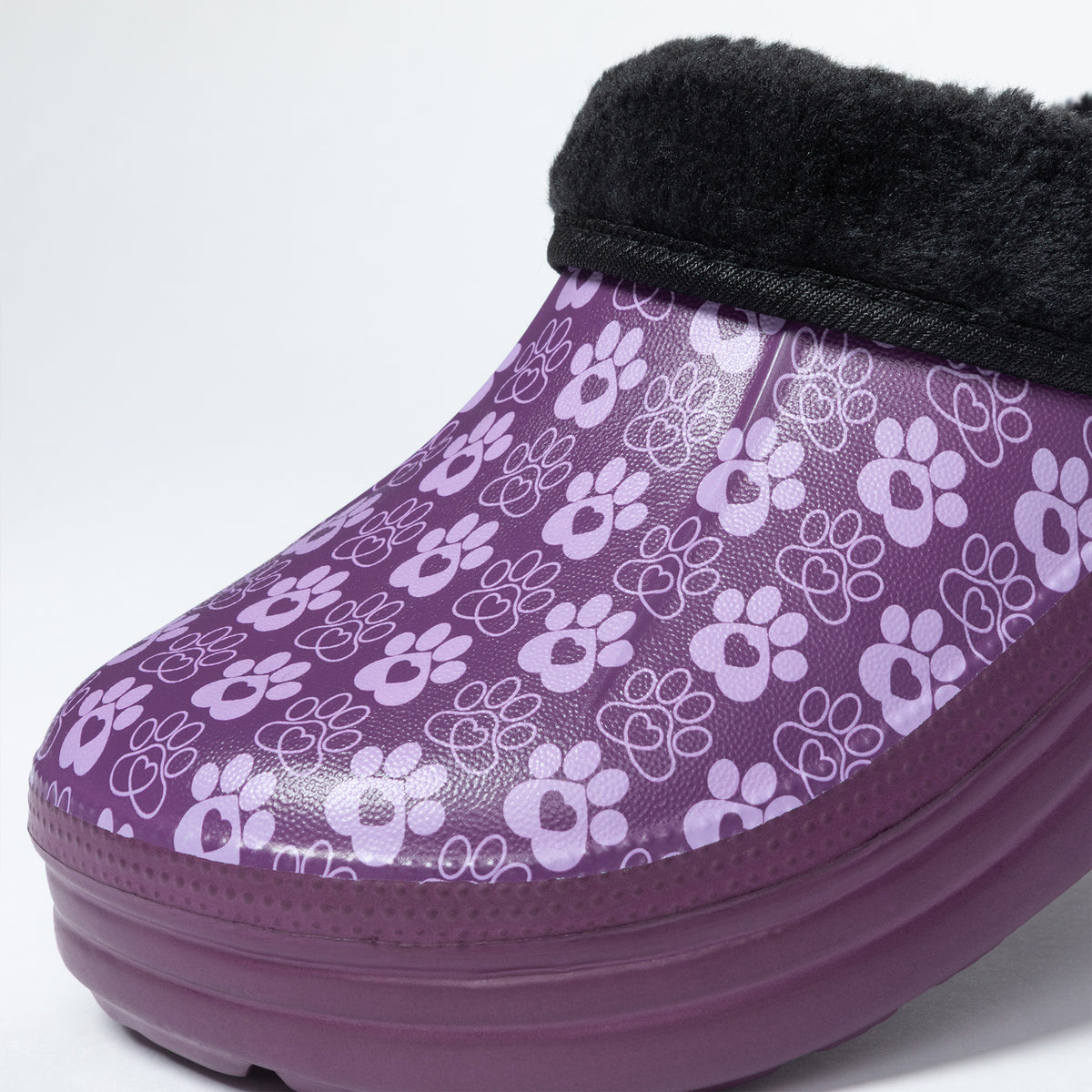 A purple slip-on clog featuring a repeating white paw print pattern, a thick purple sole, and a black faux-fur trim at the top, shown against a plain white background.
