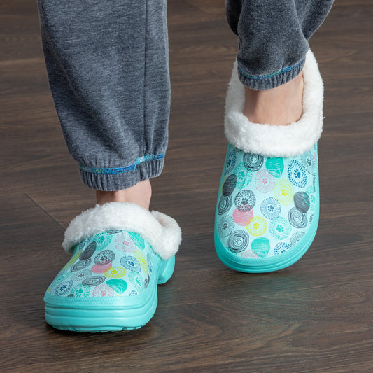Model wearing slip-on clog slippers with a paw print design, featuring a white fleece lining.