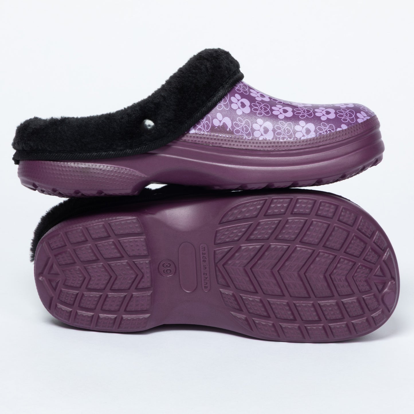 A pair of women's clogs shown on a white background, with one shoe standing upright to display the top and the other lying flat to show the sole. The top features a purple and white paw print pattern with a black faux-fur trim, while the sole is a solid dark purple with a textured tread pattern.