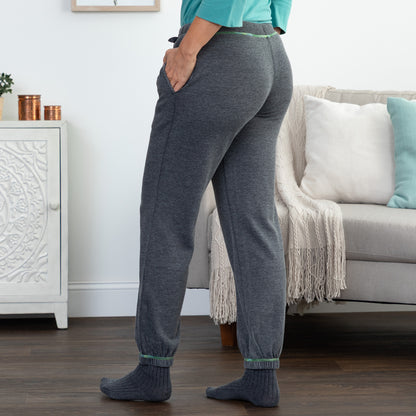 A person wearing heather dark gray jogger pants with elastic cuffs and side pockets, paired with a teal top and gray socks, standing in a living room next to a sofa.