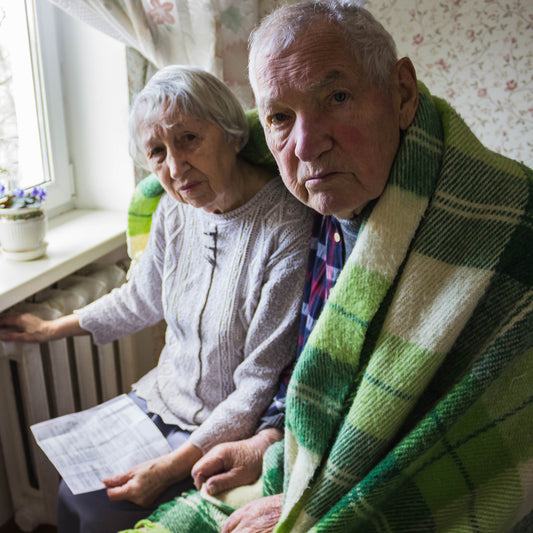 Two elderly people sitting together, one holding a piece of paper, in a home setting.