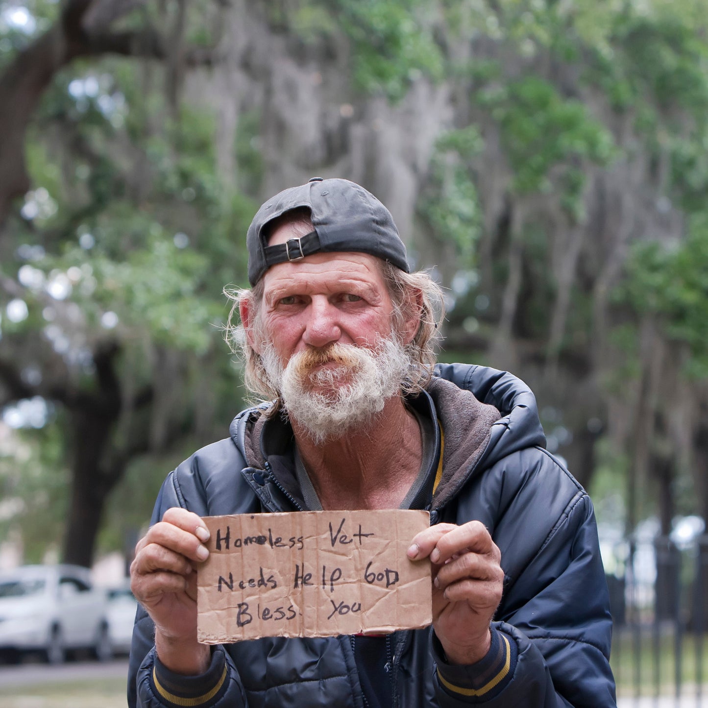 Homeless man holding a sign outdoors with trees in the background