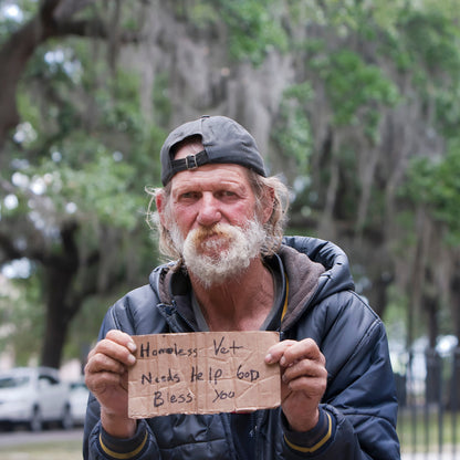 Homeless man holding a sign outdoors with trees in the background