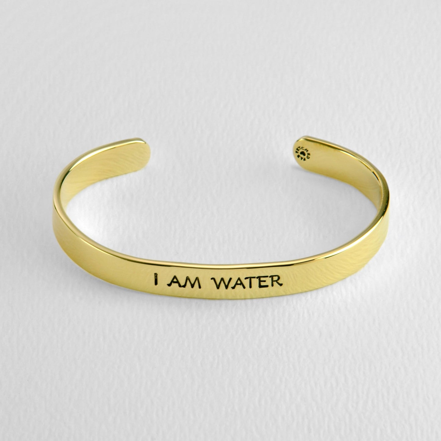 Brass bracelet with 'I AM WATER' engraving on a light gray background